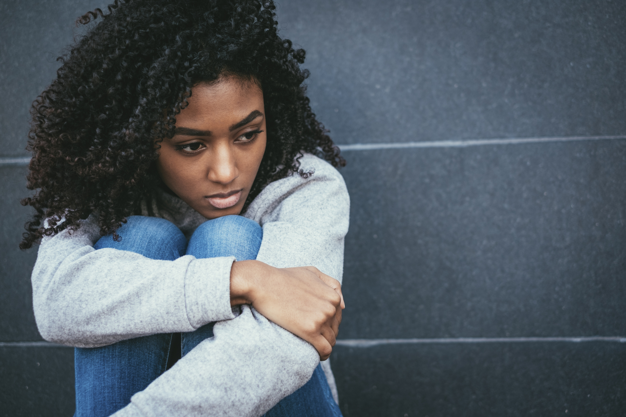 Portrait of black girl sitting down with knees tucked under chin, suffering solitude and depression