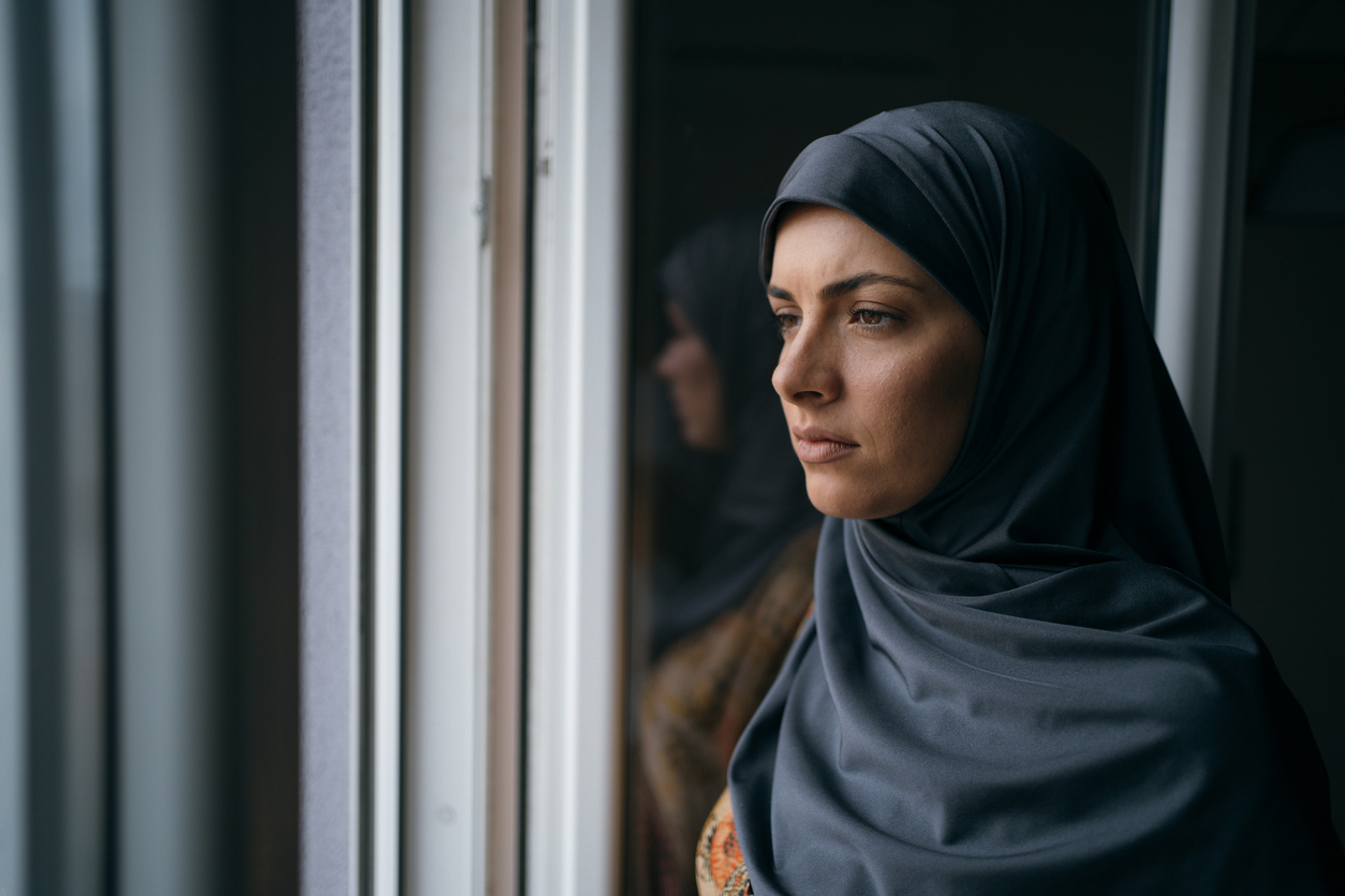 Young Muslim woman is looking worried through the window.