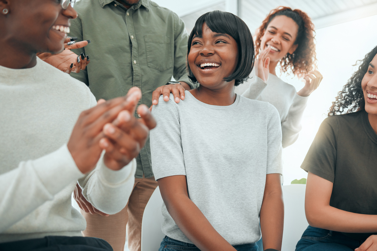 Young woman sitting while her support group celebrate her success.